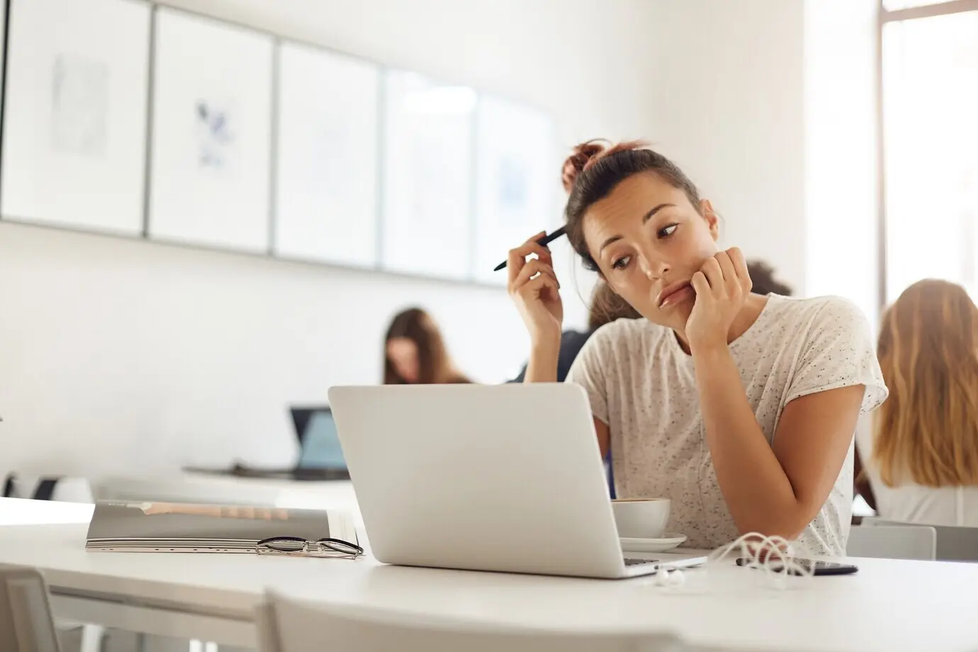 A fashion design student working on her collection, using a laptop and a magazine while drinking coffee.
